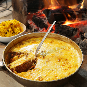 Bobotie and bowl of yellow rice by fire.